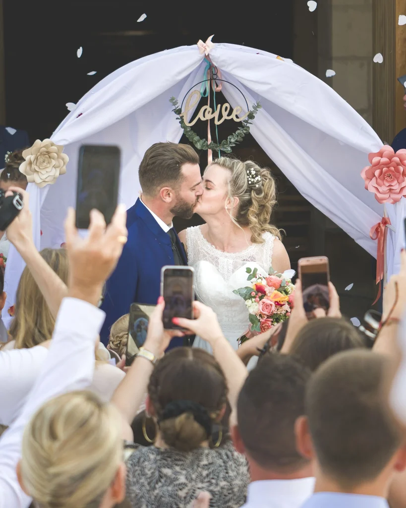 Les jeunes mariés sortent rayonnants de l’église, sous une pluie de confettis lancés par leurs invités en liesse en Bretagne. Ils s'embrasse avec passion