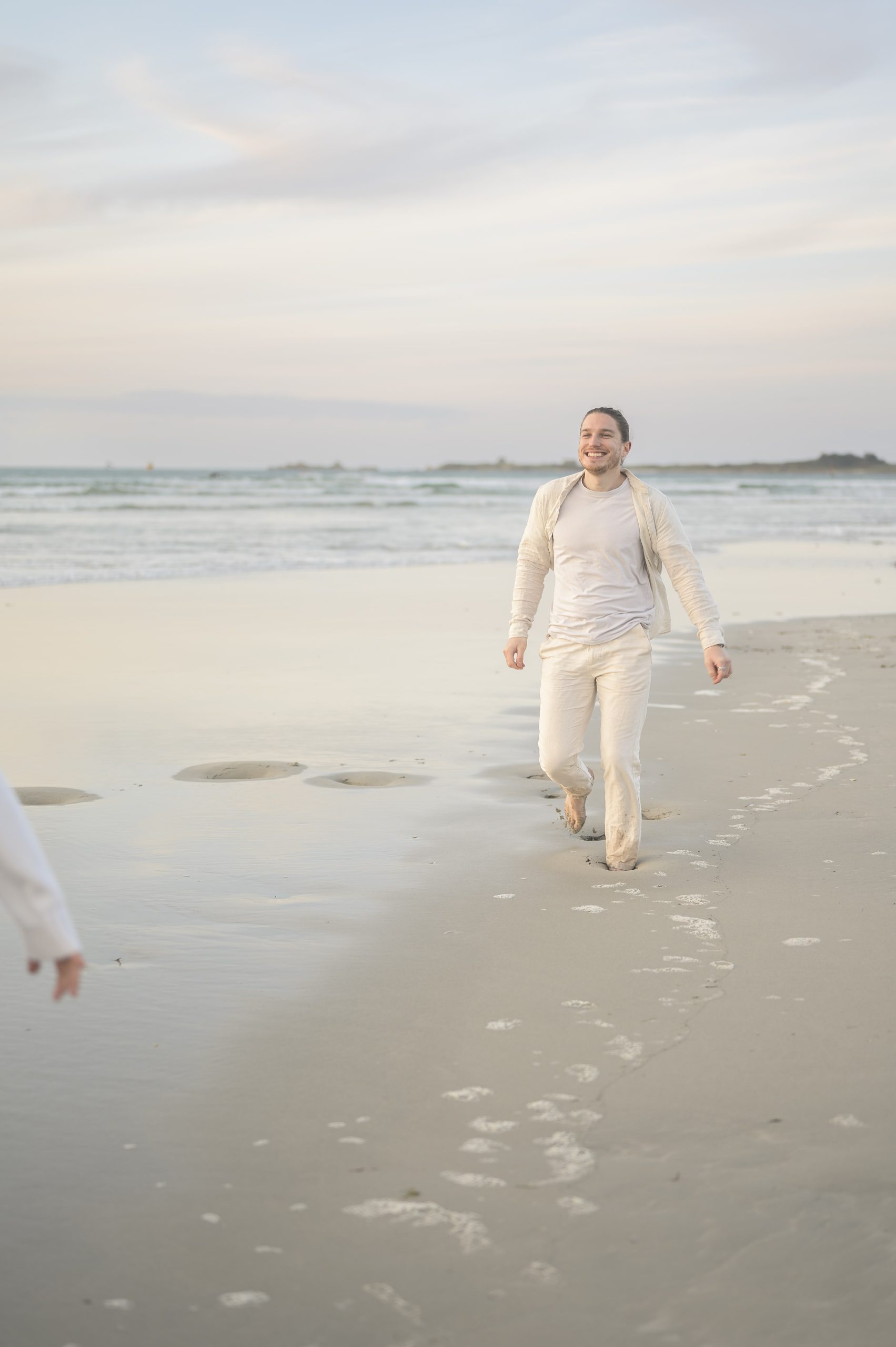 Homme-en-tenue-claire-qui-marche-pieds-nus-sur-la-plage-en-Finistère-dans-un-moment-de-joie-partagé