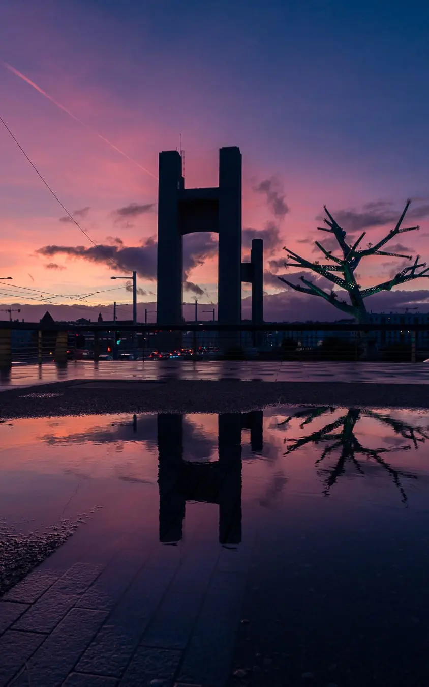 Superbe vue du pont de Recouvrance à Brest au coucher du soleil, avec un reflet dans une flaque d'eau créant une ambiance urbaine et poétique.