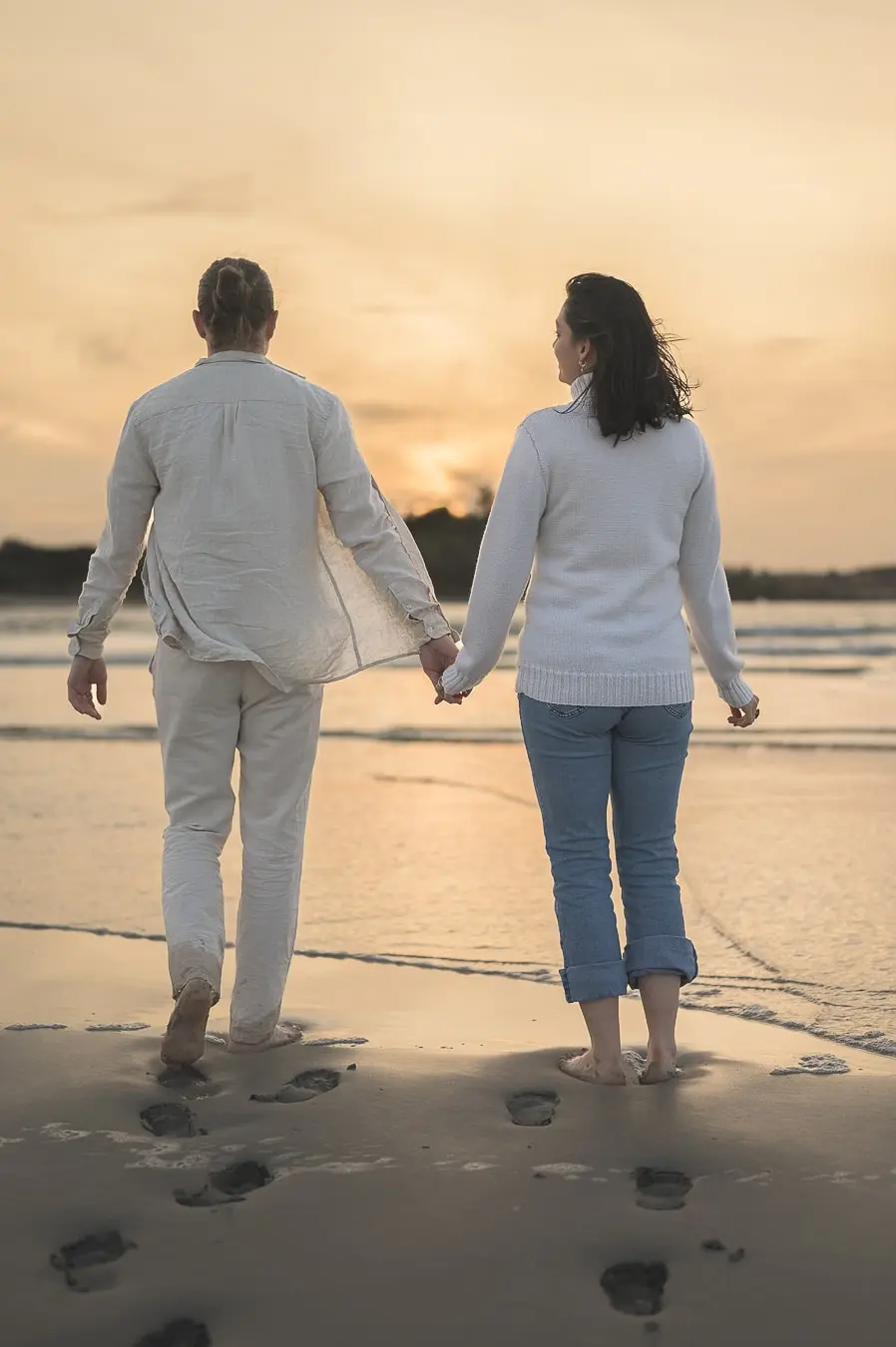 couple-de-dos-main-dans-la-main-sur-la-plage-au-coucher-du-soleil-avec-traces-dans-le-sable