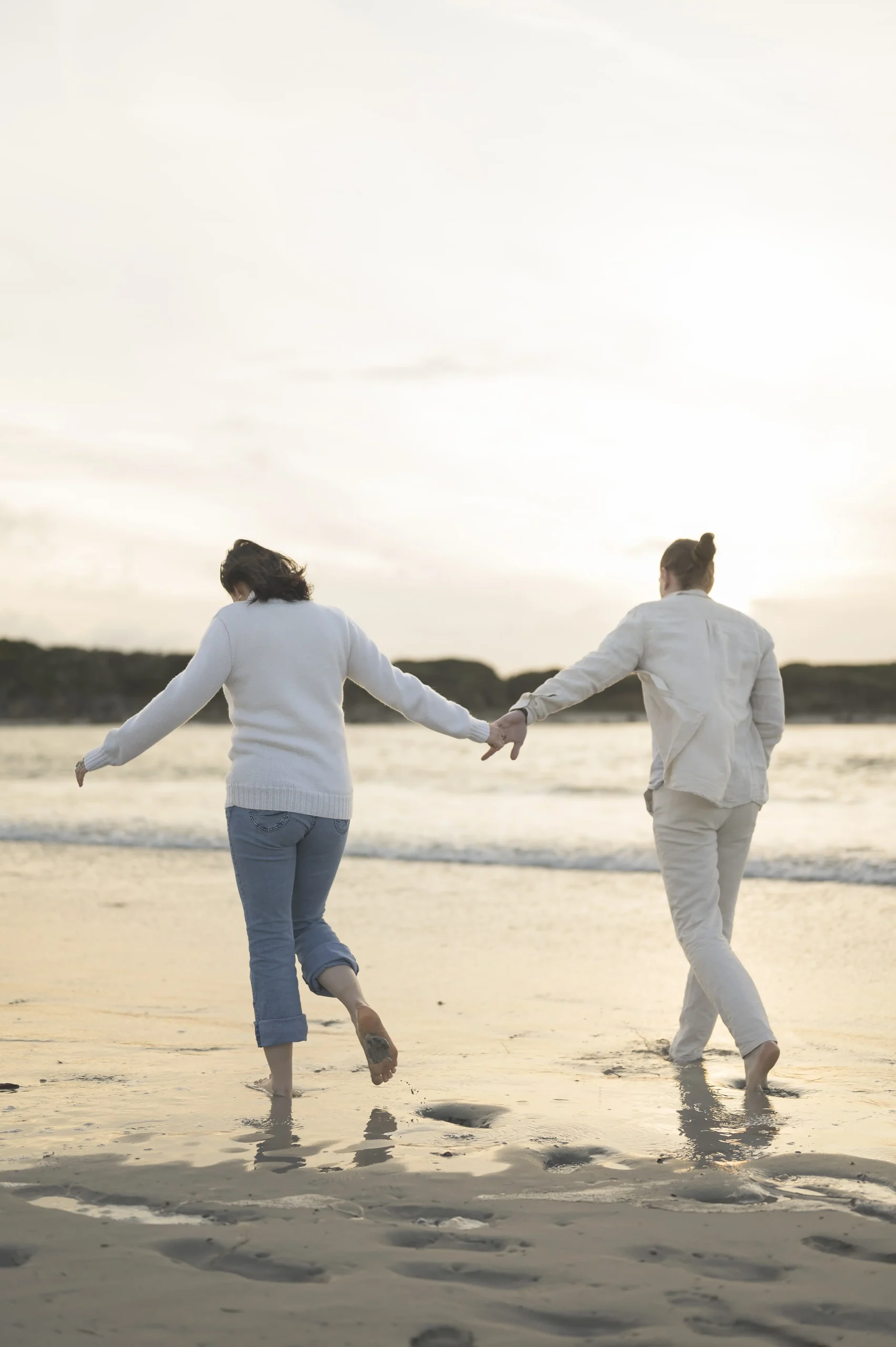 Un couple marche main dans la main sur la plage au coucher du soleil en Finistère