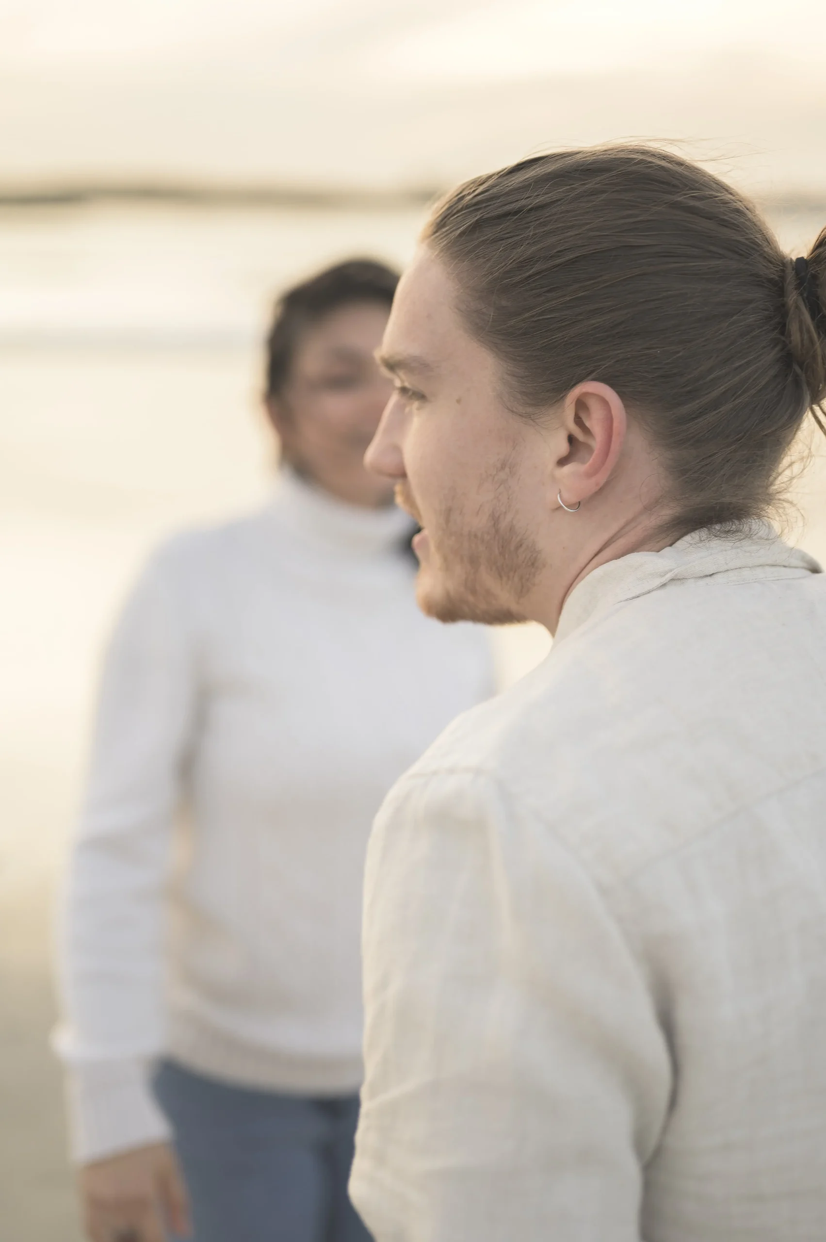 Portrait de profil d’un homme regardant sa compagne floue à l’arrière-plan, en bord de mer au coucher du soleil